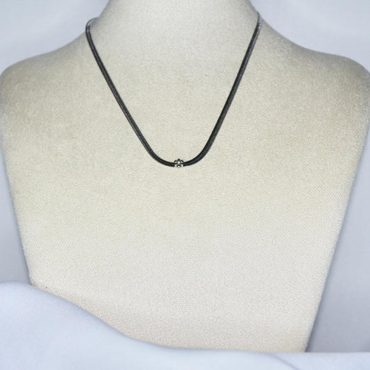 Collier modèle Vanilla Necklace en maille serpent argent avec fleur de vanille incrustée sur présentoir