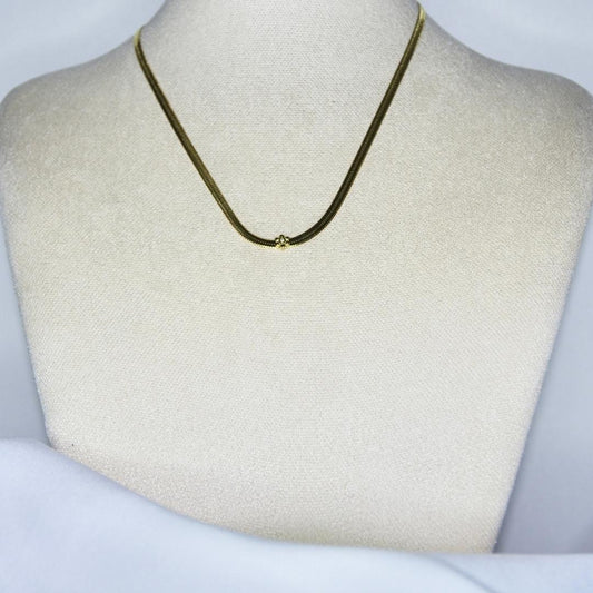 Collier modèle Vanilla Necklace en maille serpent or avec fleur de vanille incrustée sur présentoir