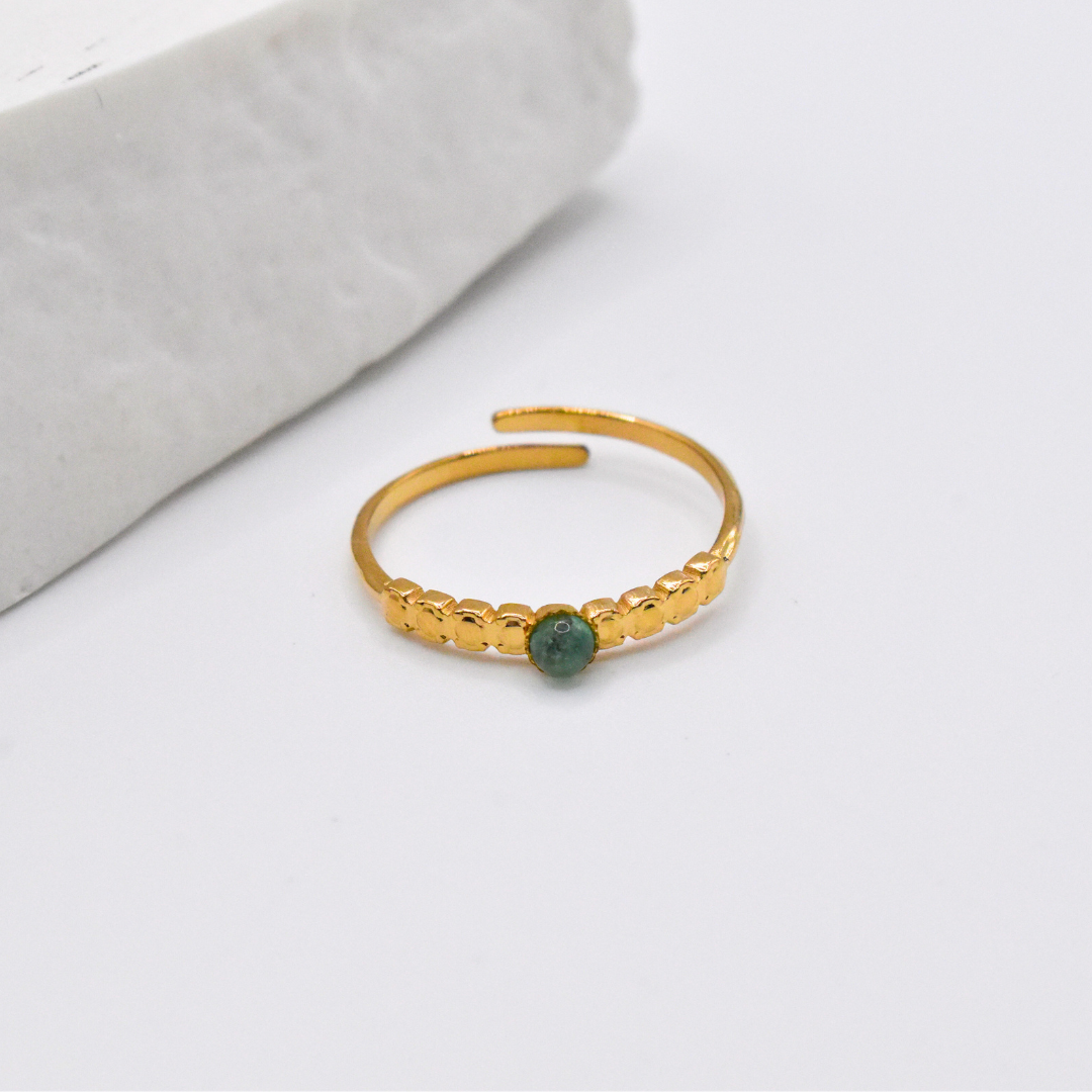 Bague modèle Dotty en or pierre verte posée près d'un support
