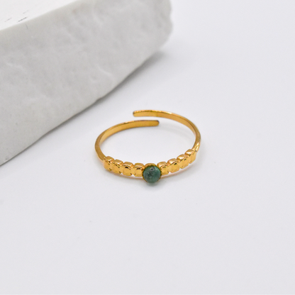 Bague modèle Dotty en or pierre verte posée près d'un support