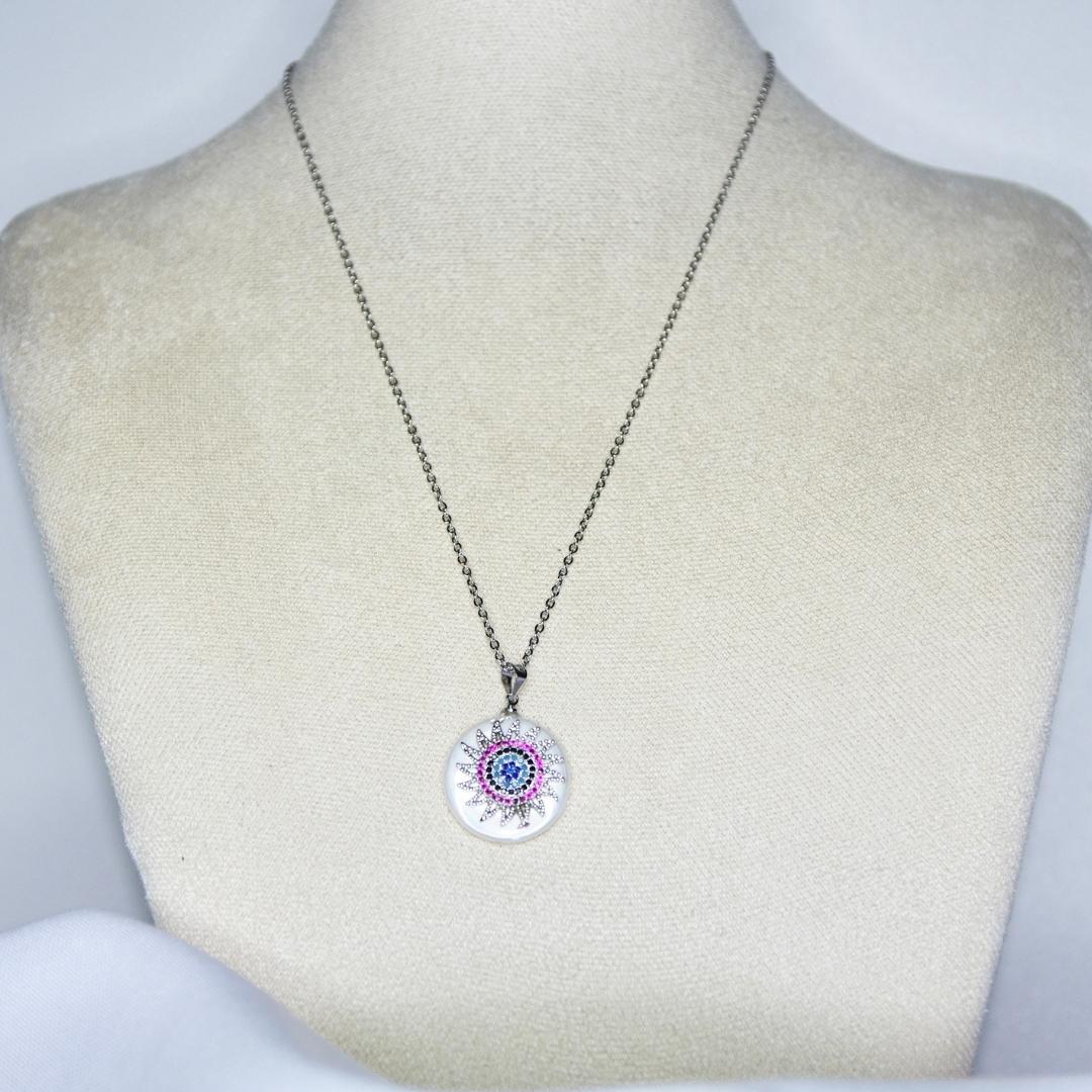 Collier modèle Sunrise Necklace en argent avec pendant soleil orné de strass colorés roses et bleus sur présentoir